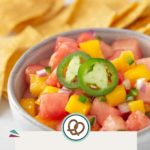 A vibrant bowl of fruit salsa features diced watermelon, mango, and onion topped with sliced jalapeños, perfectly paired with crispy tortilla chips. Text reads "Fruit Salsa" with a website link.