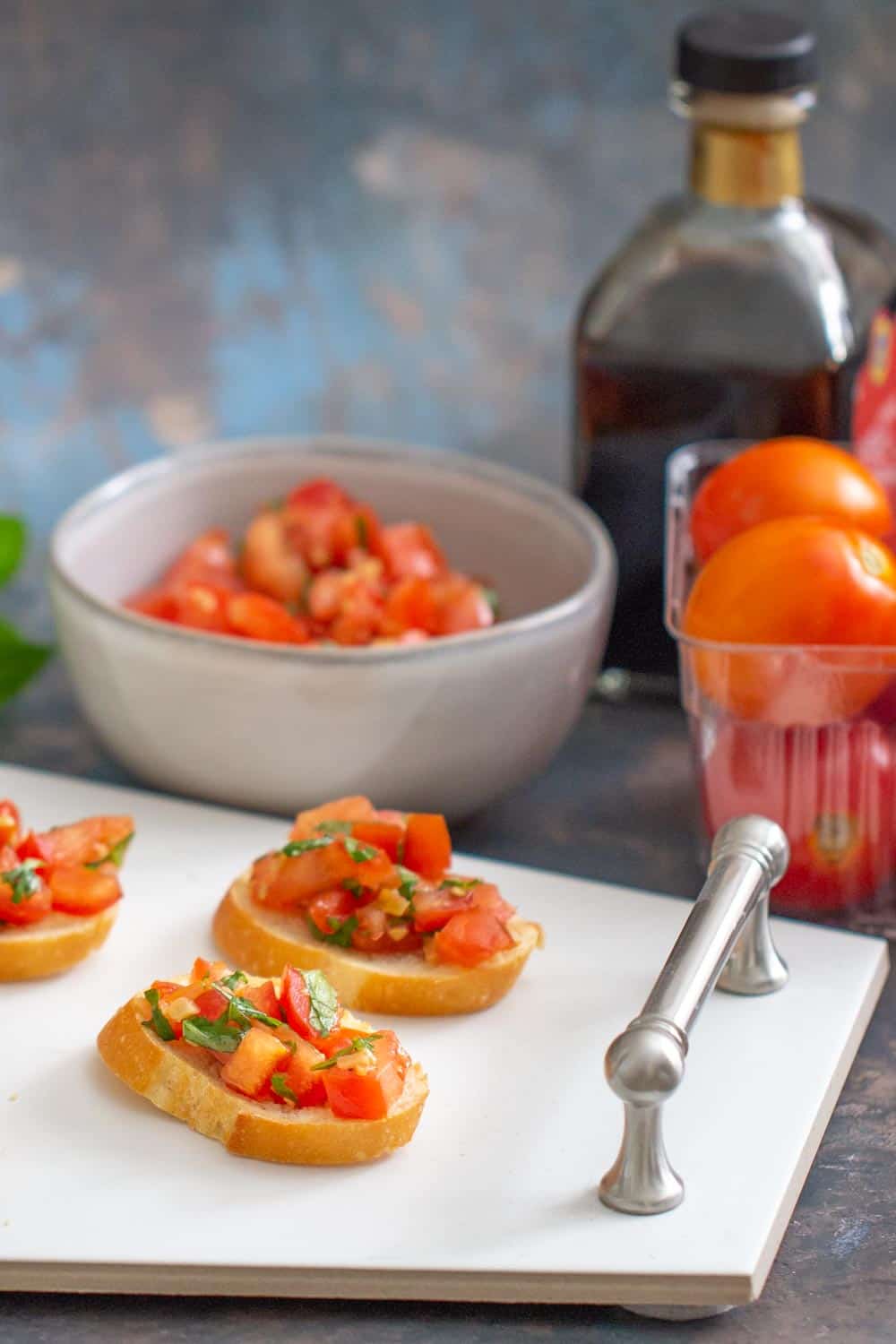 tomato bruschetta on a serving platter with ingredients behind