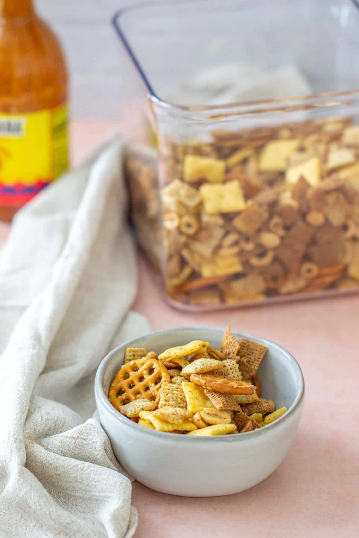 gray bowl of buffalo chex mix with large container behind
