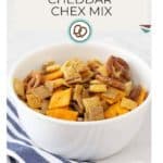 A bowl of cheddar Chex mix with pretzels and crackers sits next to a creamy beer cheese dip. The background features a striped cloth. Text reads "Homemade Recipe Cheddar Chex Mix" with a small pretzel graphic.