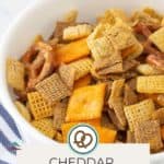 A bowl of Cheddar Chex Mix, complete with pretzels and crackers, sits ready for snacking. "Cheddar Chex Mix" reads the label at the bottom, inviting you to visit HAPPYSNACKCIDENTS.COM for more tasty creations like our beer cheese dip.