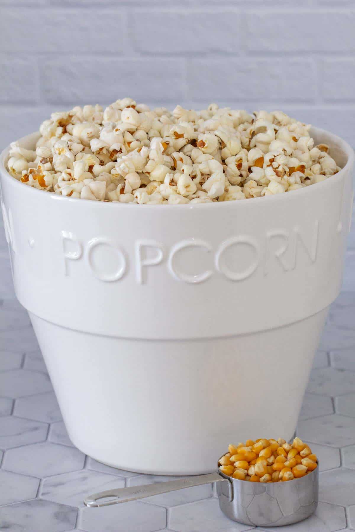 big white bowl of popped popcorn with unpopped kernels in measurig cup