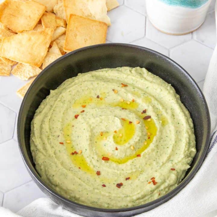 white bean dip in a black bowl with pita chips nearby for eating