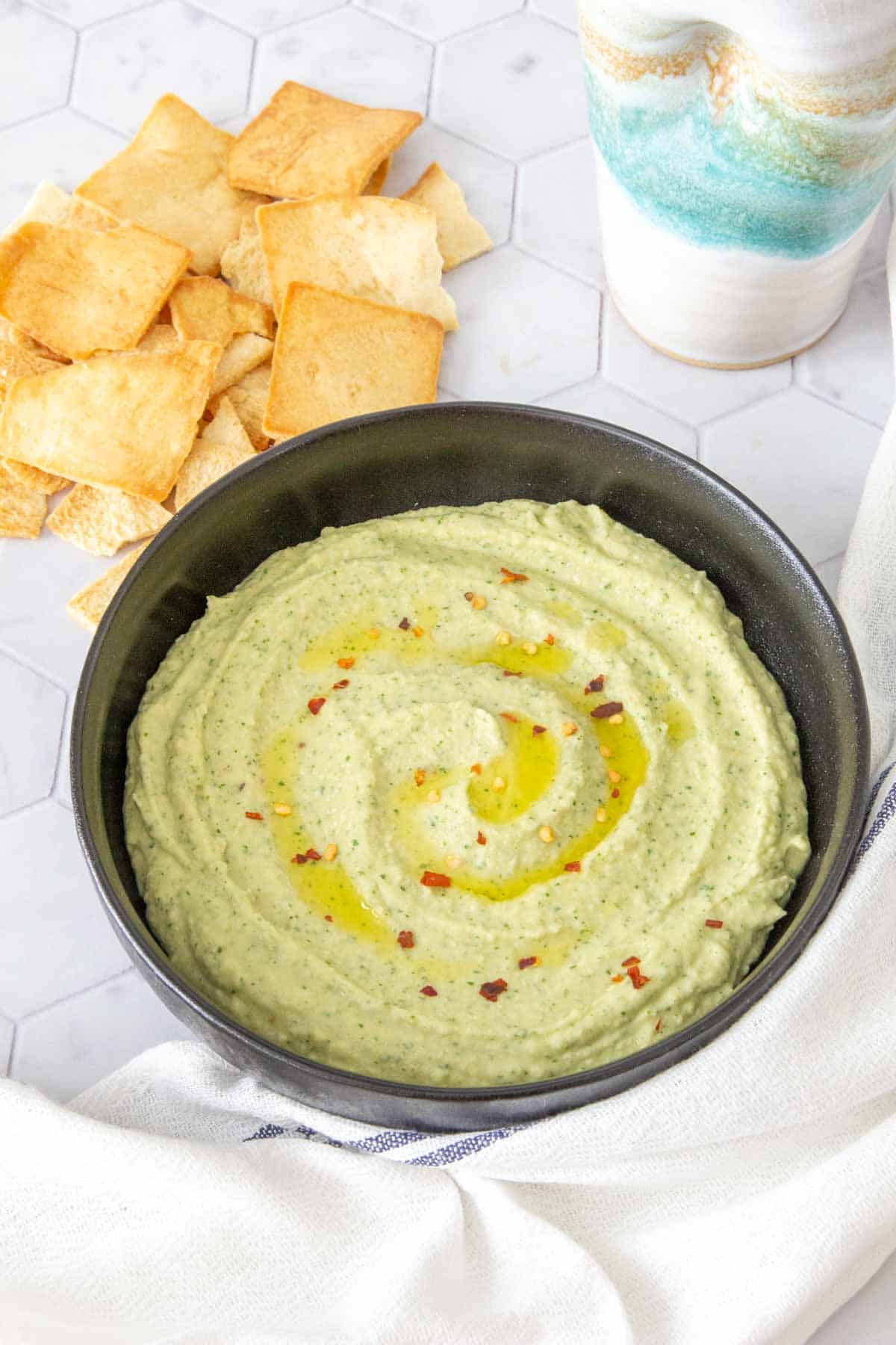 white bean dip in a black bowl with pita chips nearby for eating