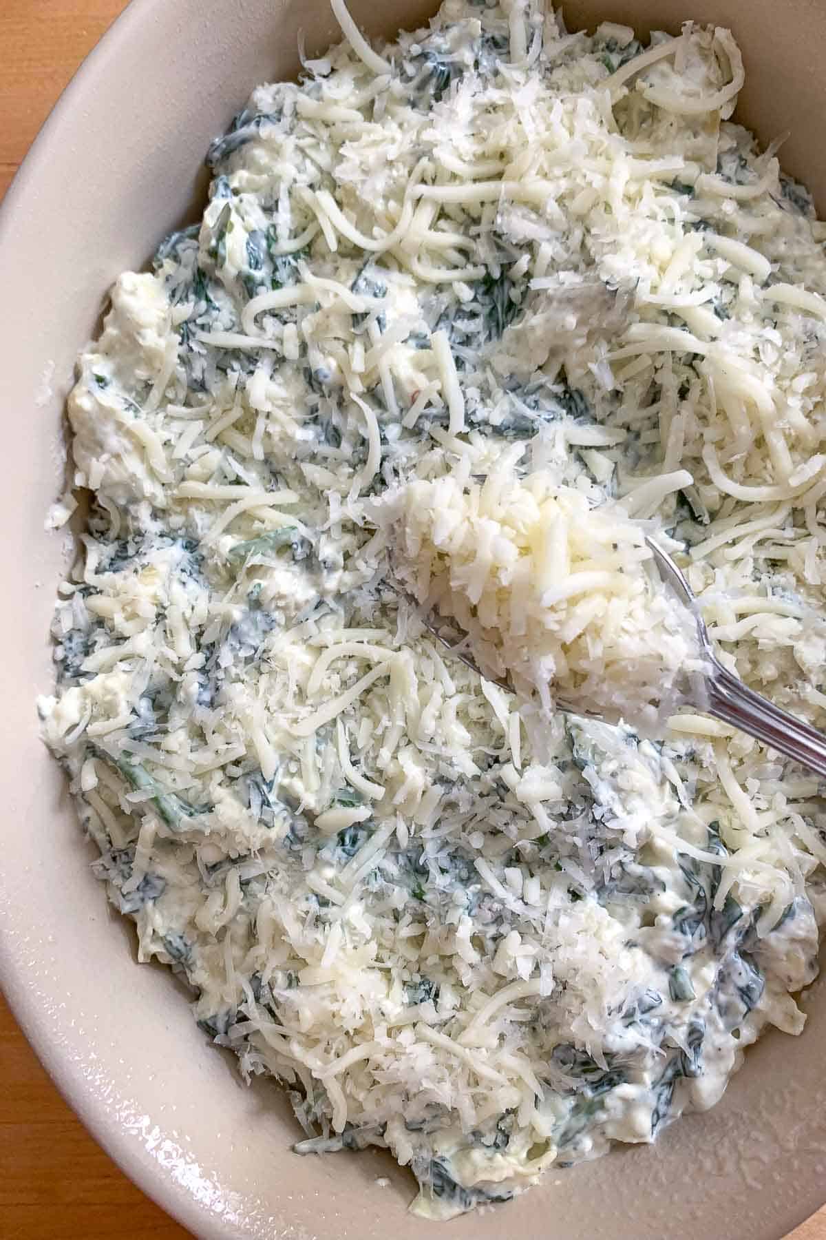 adding cheese on top of unbaked spinach artichoke dip