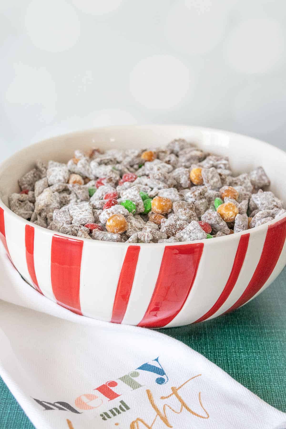 Red and white candy cane striped bowl filled with reindeer chow snack mix.