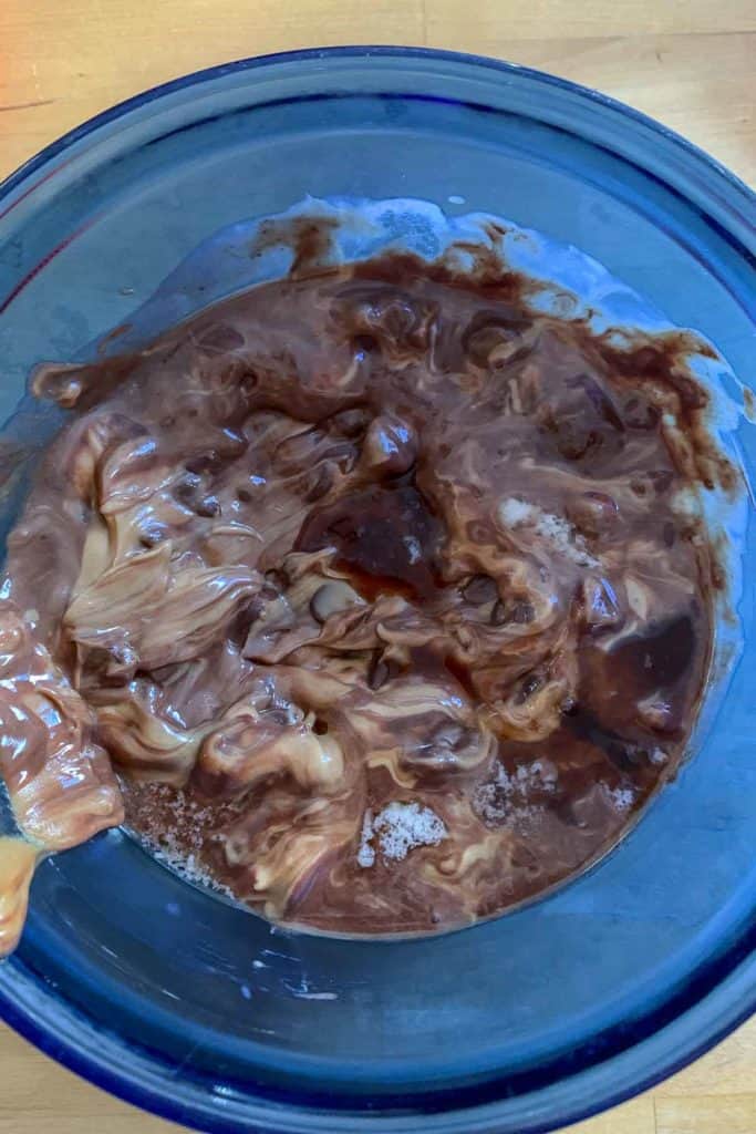 Melting together peanut butter, chocolate, and butter in a blue glass bowl.