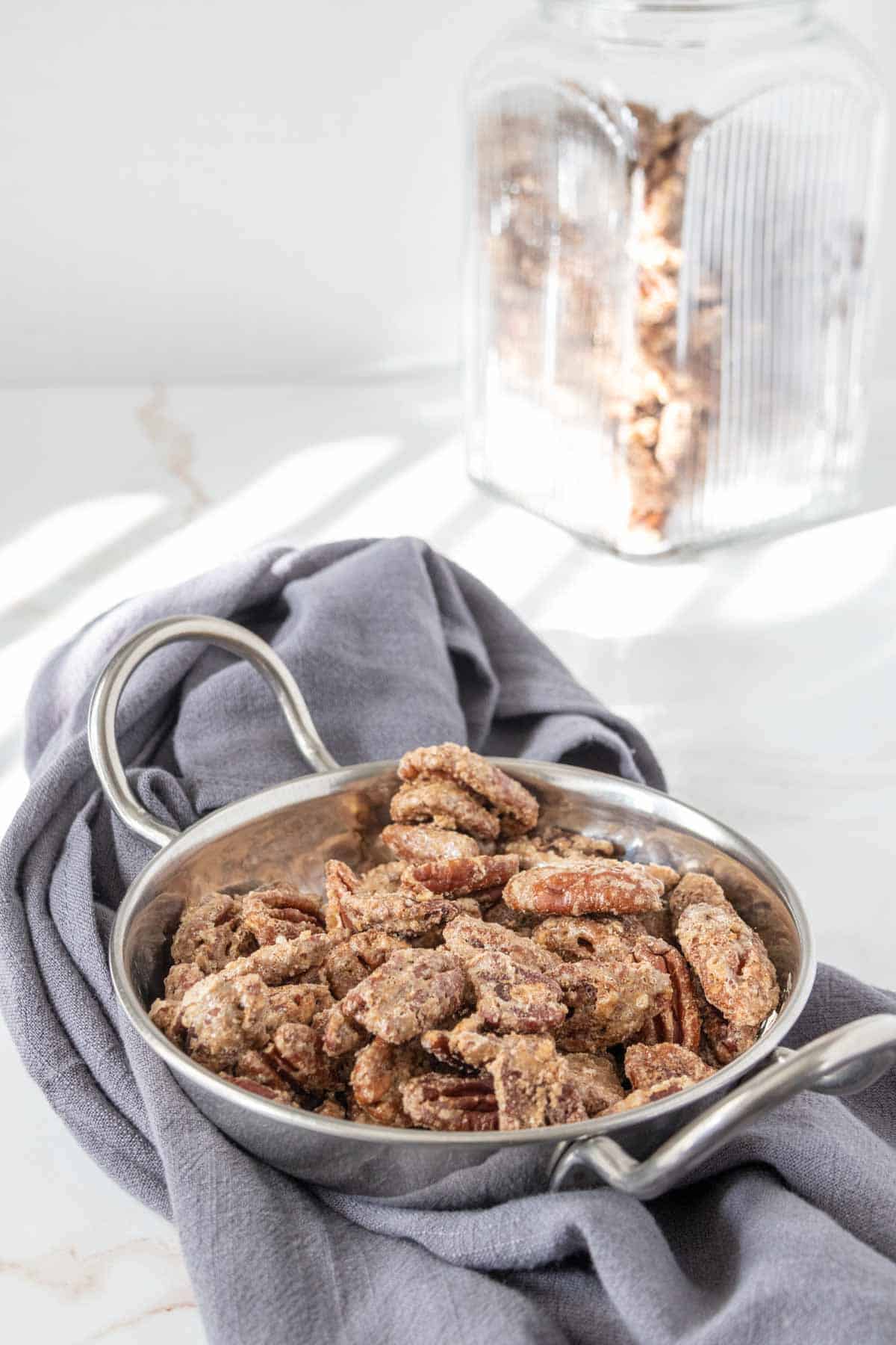 Bowl of candied pecans with glass container behind.