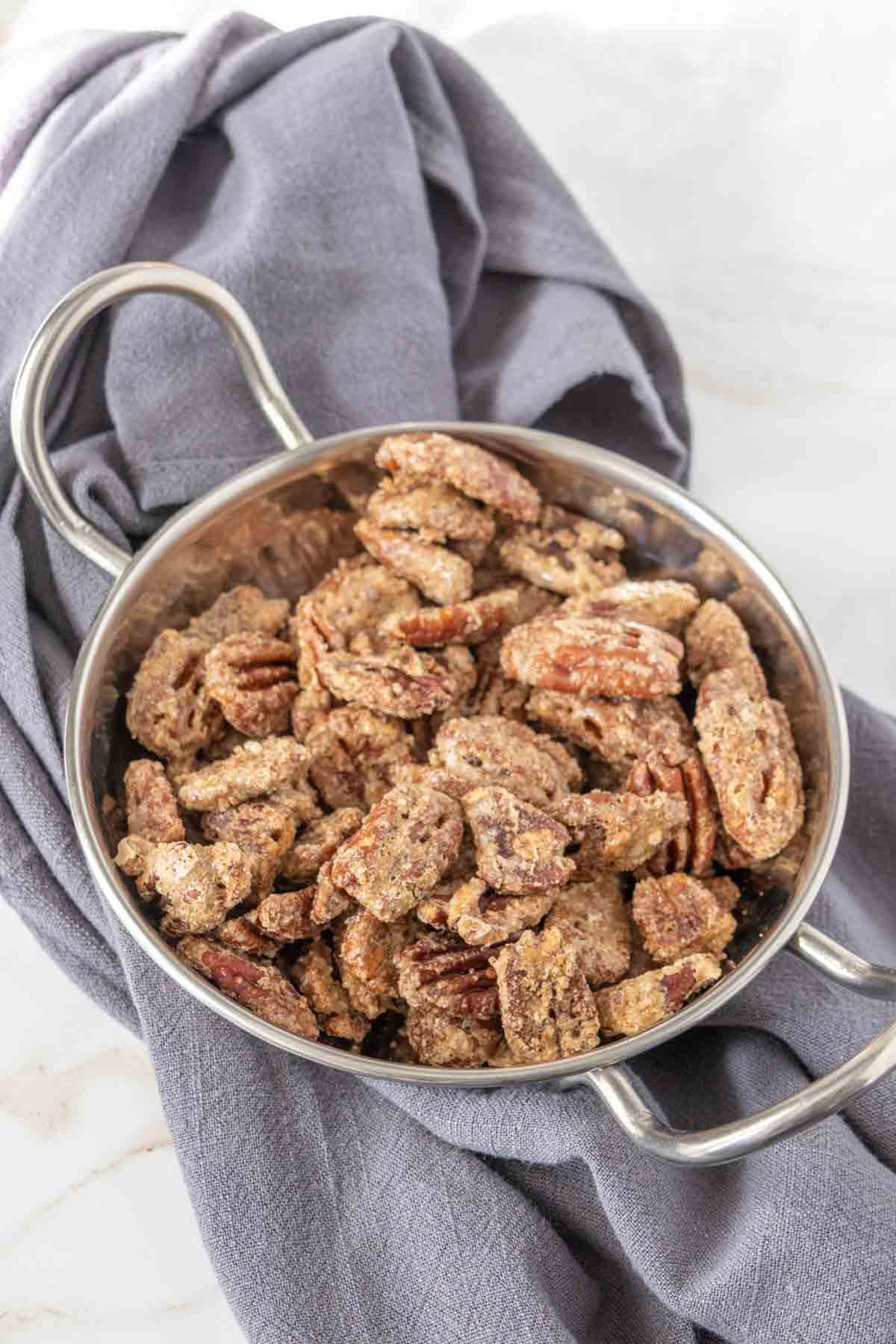 Small silver bowl filled with candied pecans on a gray napkin.