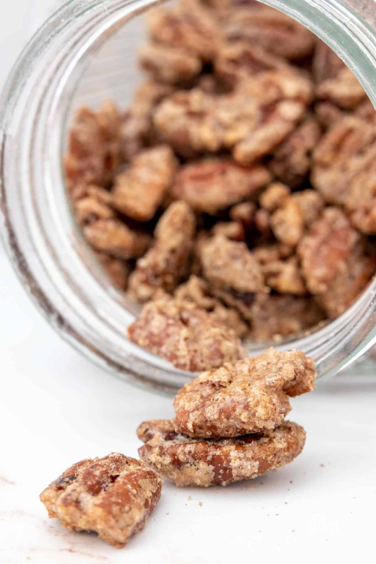 Candied pecans poured out of a glass container.