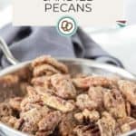 A metal pan filled with candied pecans rests on a gray cloth, featuring a label that reads "Candied Pecans" and a website URL at the bottom.