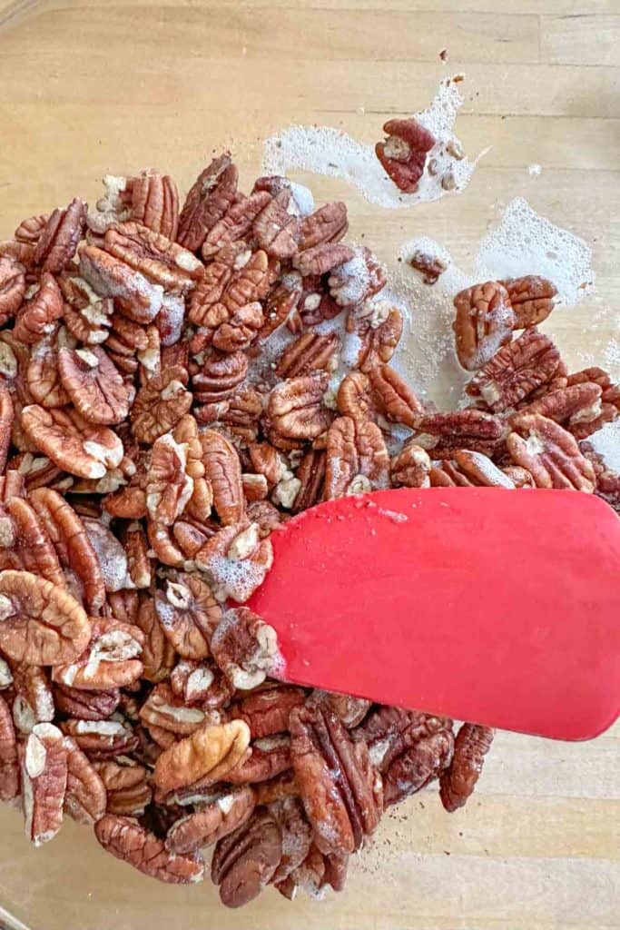 Mixing pecans with egg white in a glass mixing bowl.