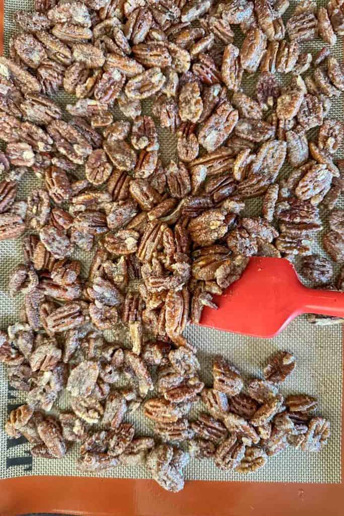 Stirring candied pecans on baking sheet with spatula.