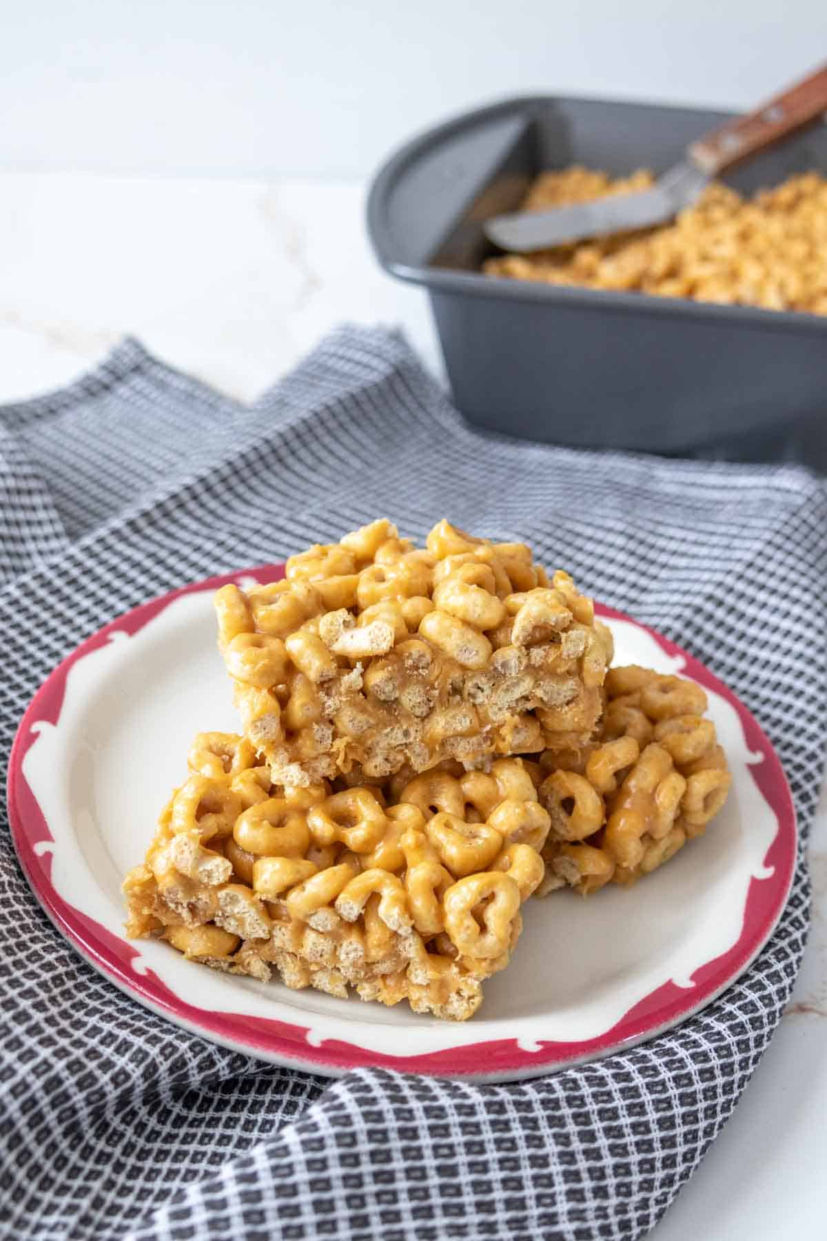 Three cereal bars stacked on a plate with the rest of the pan behind.