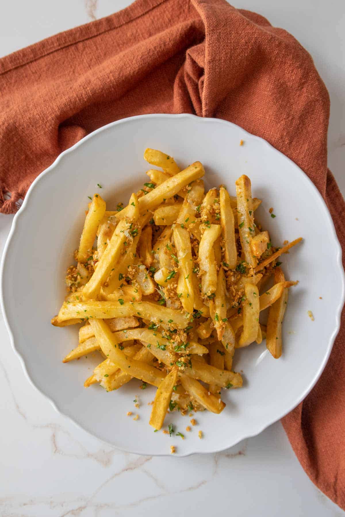 Garlic fries in a white bowl with a rust colored kitchen towel underneath.