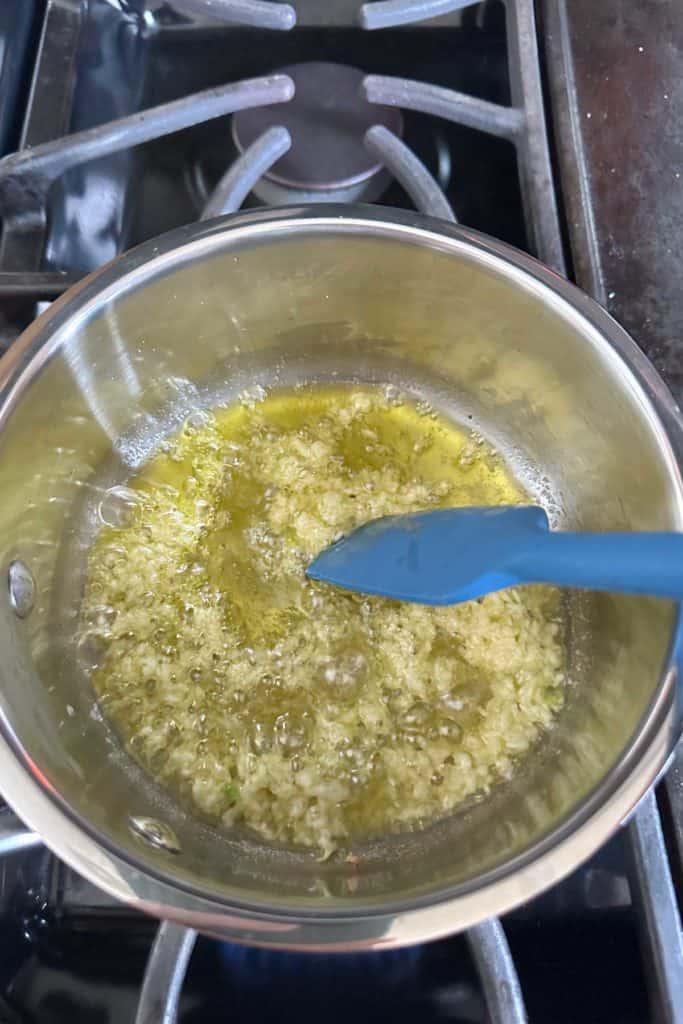 Garlic being sauteed in olive oil in a small saucepan.