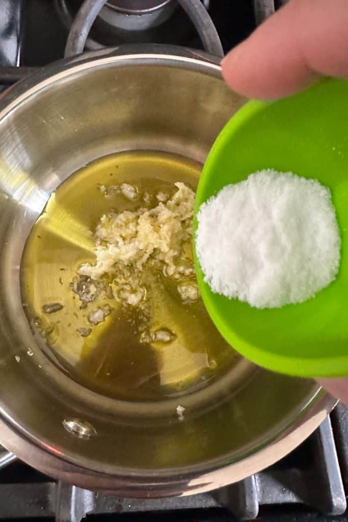 Saucepan with olive oil, garlic, and salt being added.