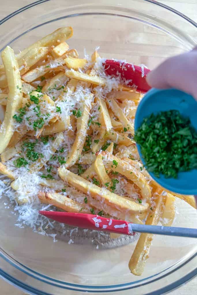 Chopped parsley being added to a bowl of garlic fries.