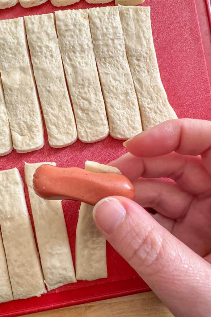 Wrapping crescent dough around a cocktail sausage.