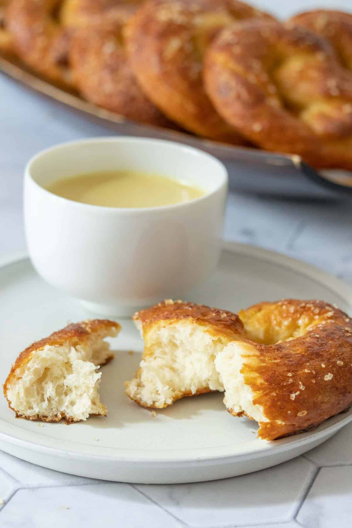 Ripped pretzel pieces on a plate with sauce in a cup.