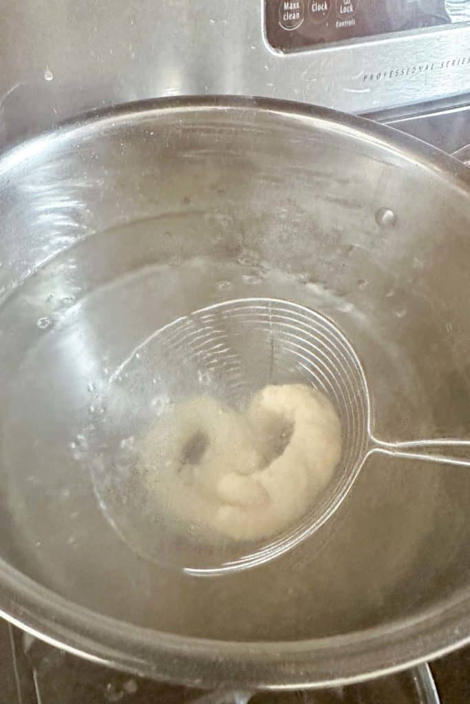 Lowering pretzel dough into water for boiling.