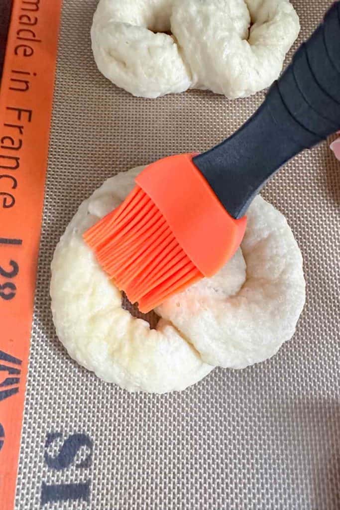 Brushing egg wash onto boiled pretzels.