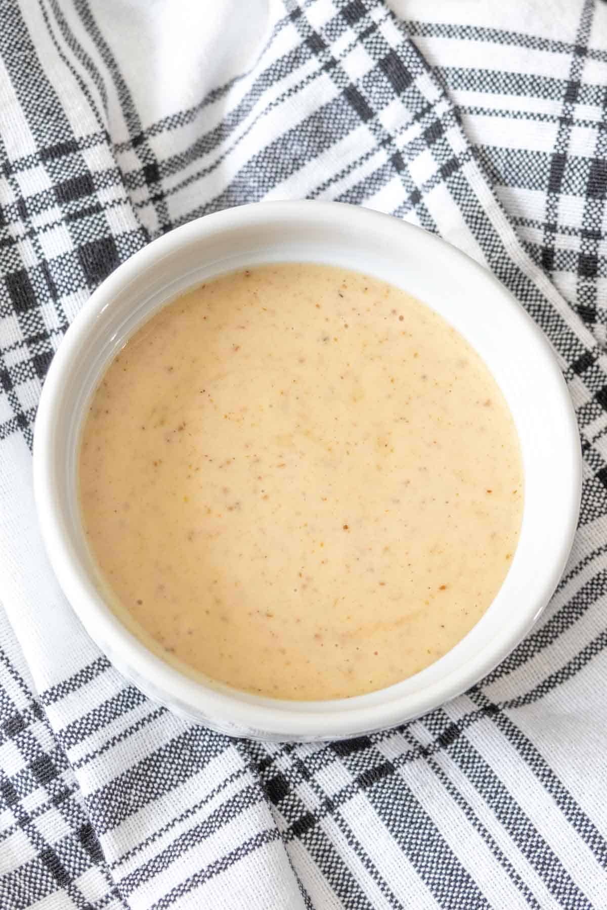 Bowl of dipping sauce in a white bowl on a black and white napkin.