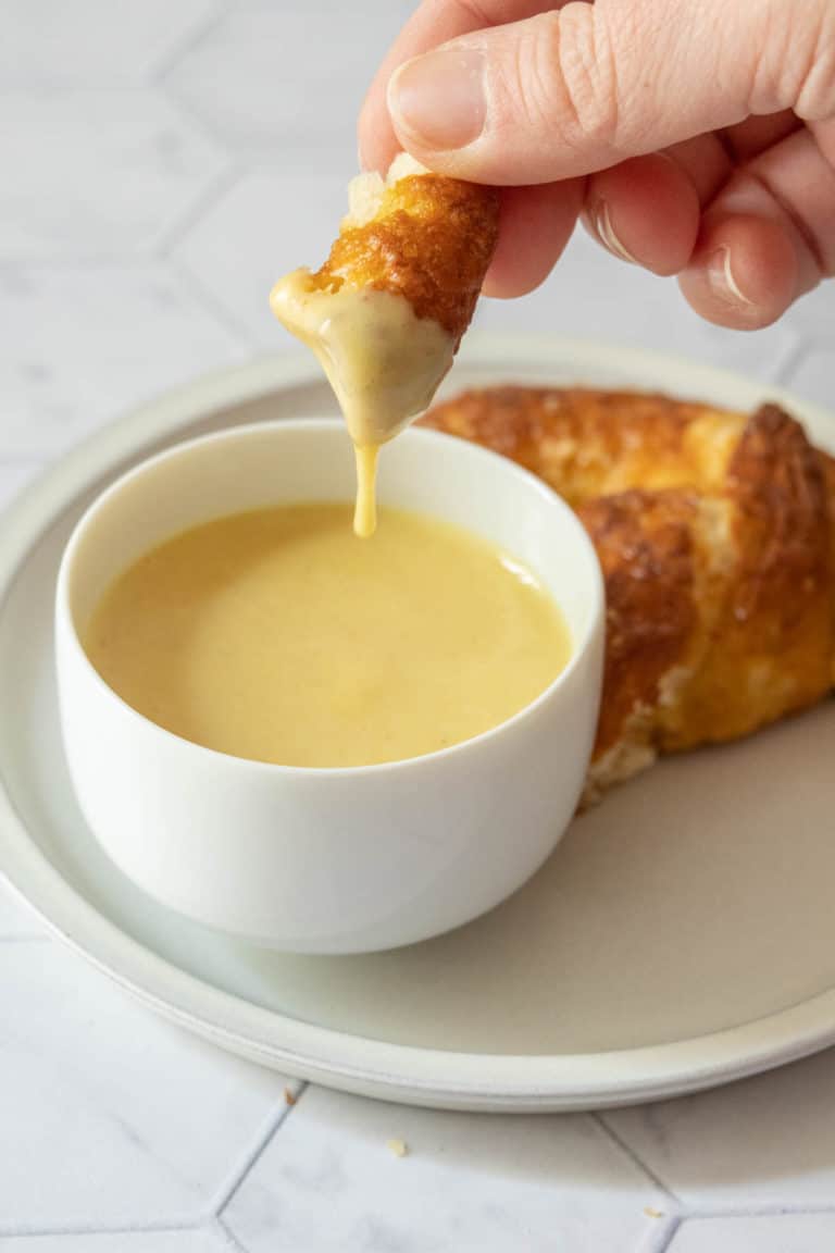Hand holding a piece of pretzel with honey mustard sauce dripping off.