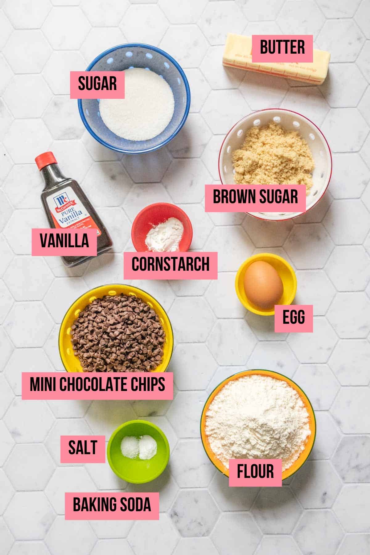 Ingredients for mini chocolate chip cookies on a tile surface with labels.