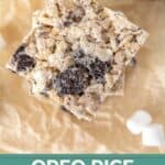 A close-up of Oreo Rice Krispie treats stacked on parchment paper, with visible Oreo cookie pieces and mini marshmallows, and text reading "Oreo Rice Krispie Treats" for the perfect sweet snack.
