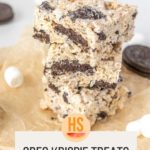 A stack of Oreo Rice Krispie Treats sits on parchment paper, surrounded by marshmallows and cookies. A label reads "Oreo Krispie Treats - happysnackcidents.com.