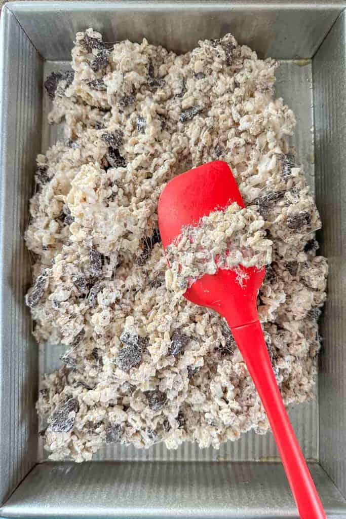 Pressing Oreo rice krispie treats into a pan with a red spatula.