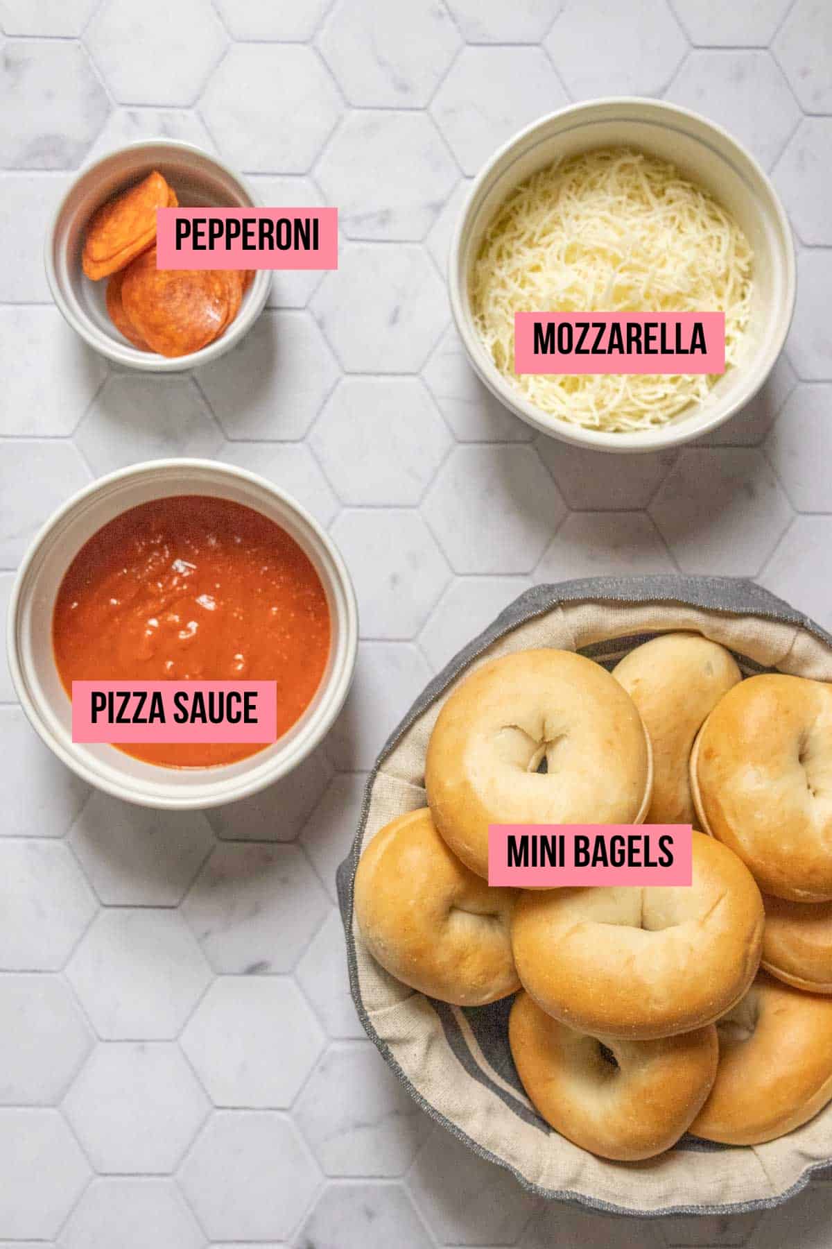 Ingredients for pizza bagel bites on a tile surface with labels.