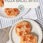 Two plates filled with cheesy, pepperoni-topped pizza bagel bites rest on a striped cloth over a wooden surface. Text reads "Pizza Bagel Bites" and "happysnackcidents.com." Perfect for satisfying any pizza craving!.