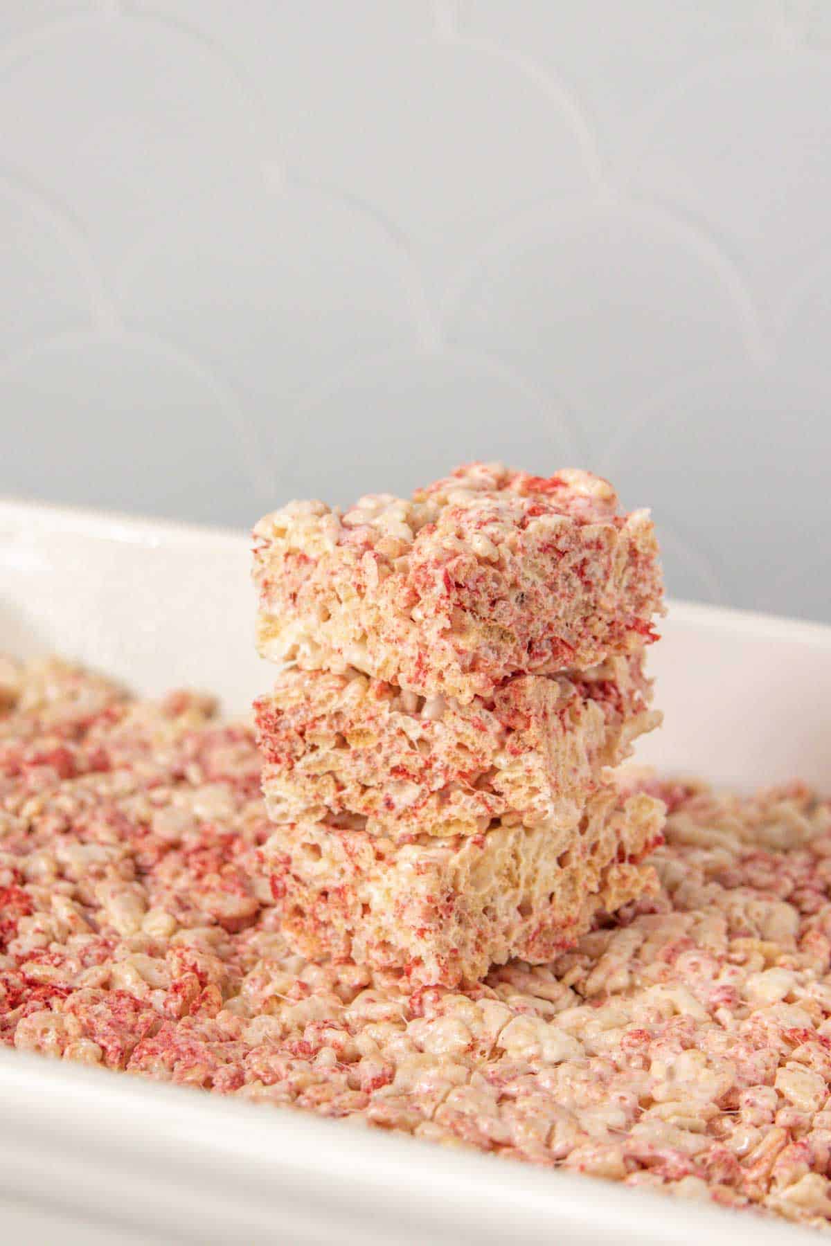 Stack of strawberry rice krispie treats on top of treats in pan.