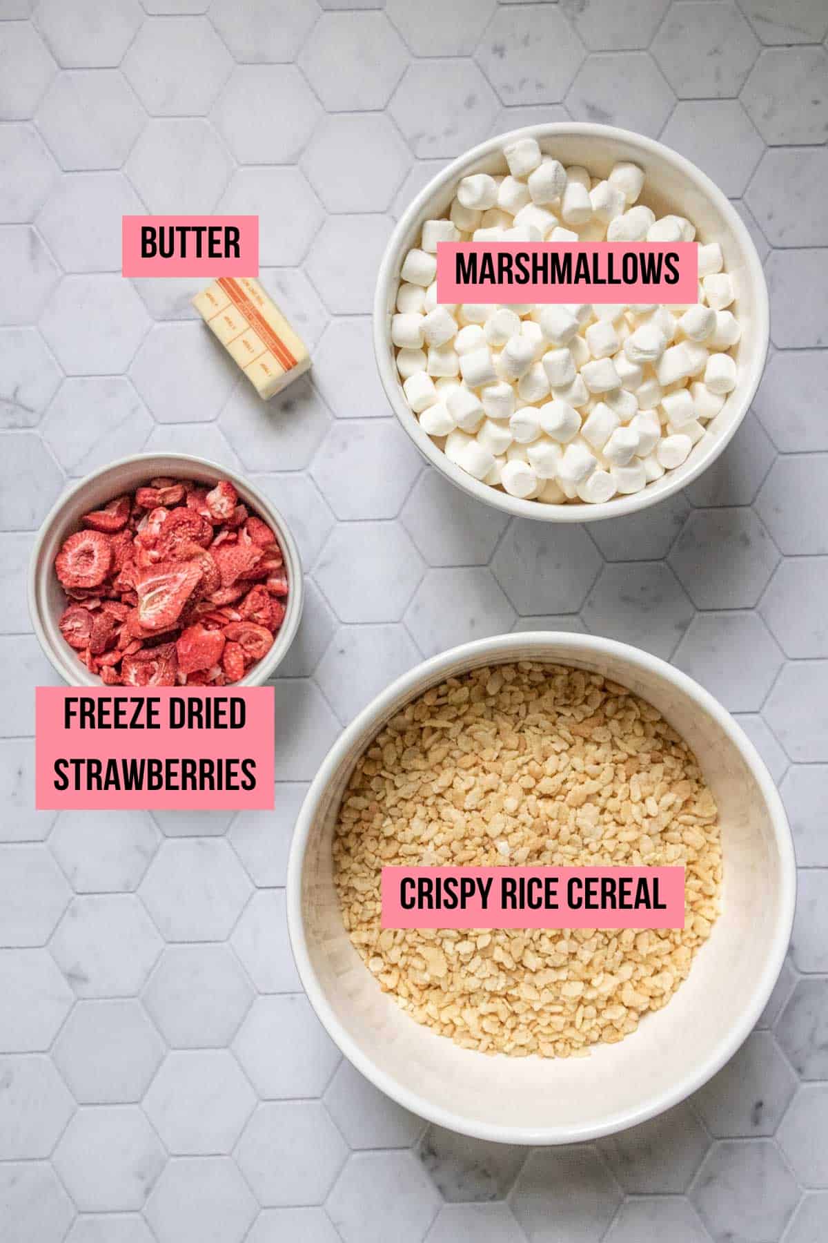 Ingredients for strawberry rice krispie treats on a tile surface with labels.