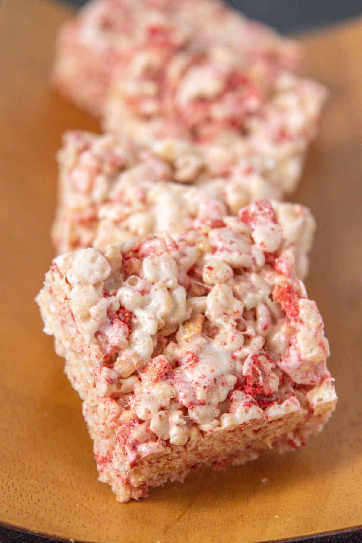 Line of strawberry rice krispie treats on a wooden tray.