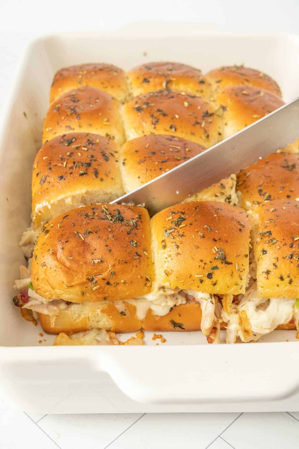 Chicken sliders in a baking dish with a knife.