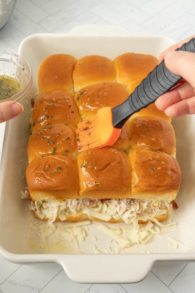 A person brushing melted butter and herbs on slider buns.