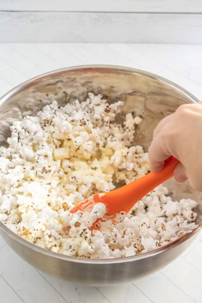 A person mixing popcorn in a bowl with an orange spatula.