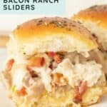 Close-up of chicken bacon ranch sliders on a plate, with creamy filling and diced bacon between golden, seasoned buns.