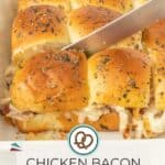 A knife slices into a tray of golden, herb-topped chicken bacon ranch sliders, each one filled with savory chicken and crispy bacon on soft pull-apart rolls.
