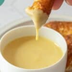 A hand dips a pretzel stick into creamy honey mustard sauce, with the golden sauce dripping off. Text on image reads "Honey Mustard Sauce" and "happysnackcidents.com".