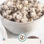 A ceramic bowl filled with Oreo popcorn sits on a white surface; two Oreo cookies and a napkin are nearby, making this the perfect snack for any cookies-and-cream lover.