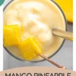 A glass of mango pineapple smoothie with two metal straws and a garnish of pineapple chunks, shown from above. Text reads "Mango Pineapple Smoothie - HappySnackcidents.com"—the perfect tropical mango pineapple smoothie treat.