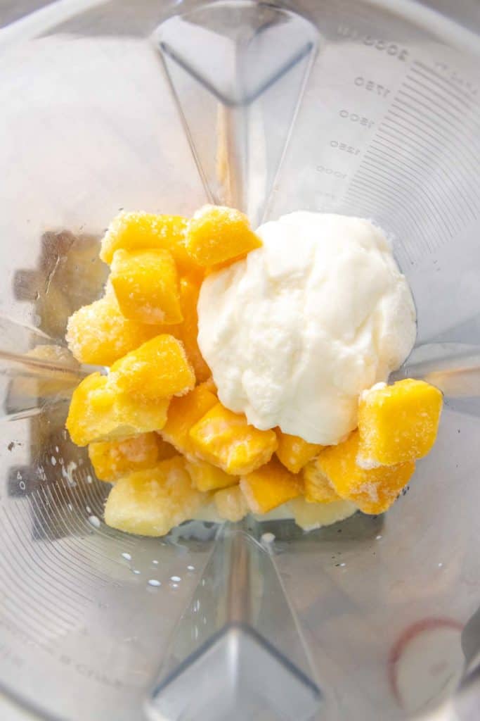 Chunks of frozen mango and a scoop of yogurt in a blender.