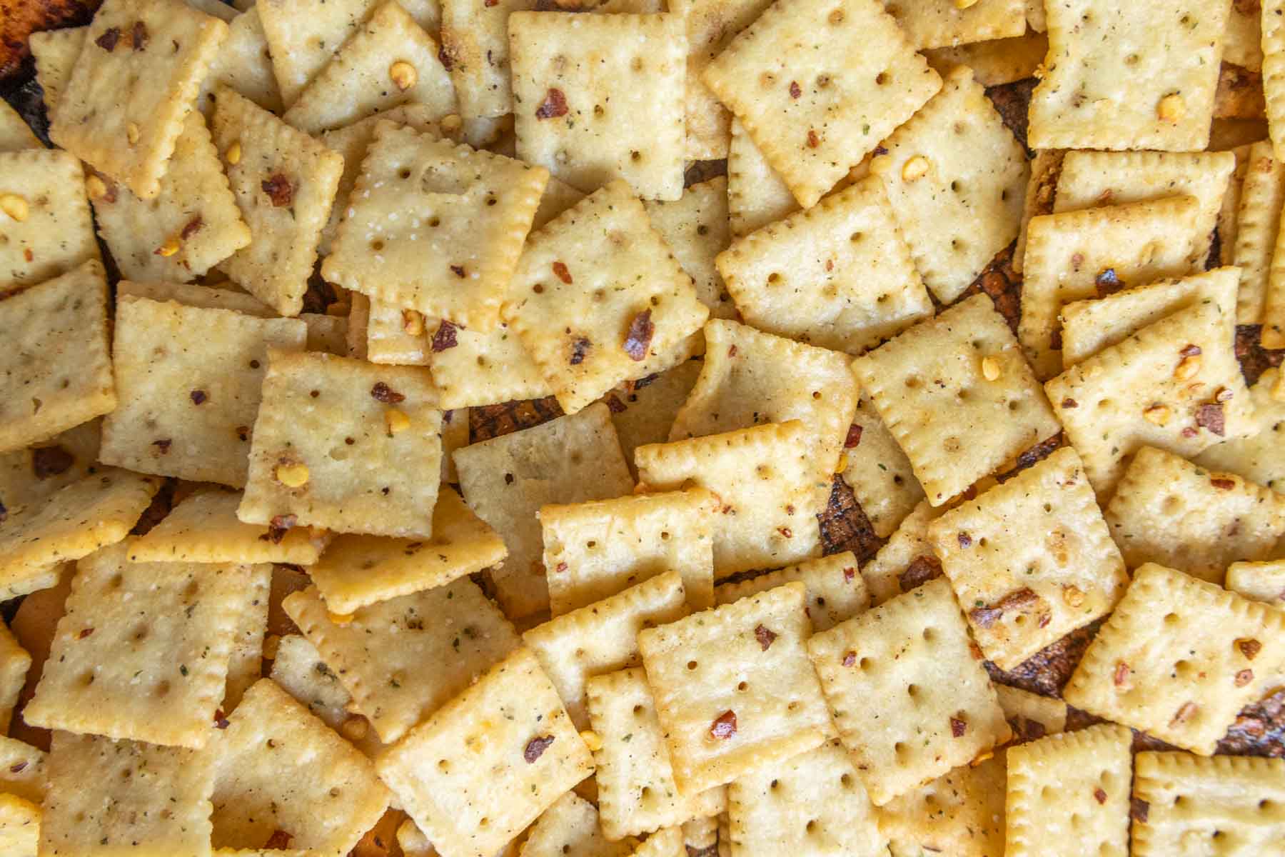 A pile of square crackers seasoned with visible specks of spices.