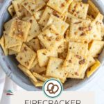 A bowl filled with square firecracker crackers topped with red pepper flakes, featuring a label at the bottom that reads "Firecracker Crackers happysnackcidents.com.
