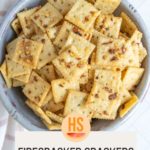 A bowl of square crackers topped with spices, labeled "Firecracker Crackers" with a website link below.