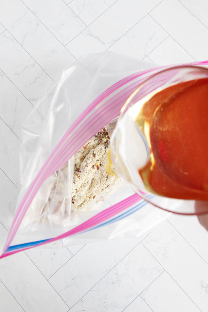 Pouring liquid into a resealable plastic bag containing dry ingredients on a white tiled surface.